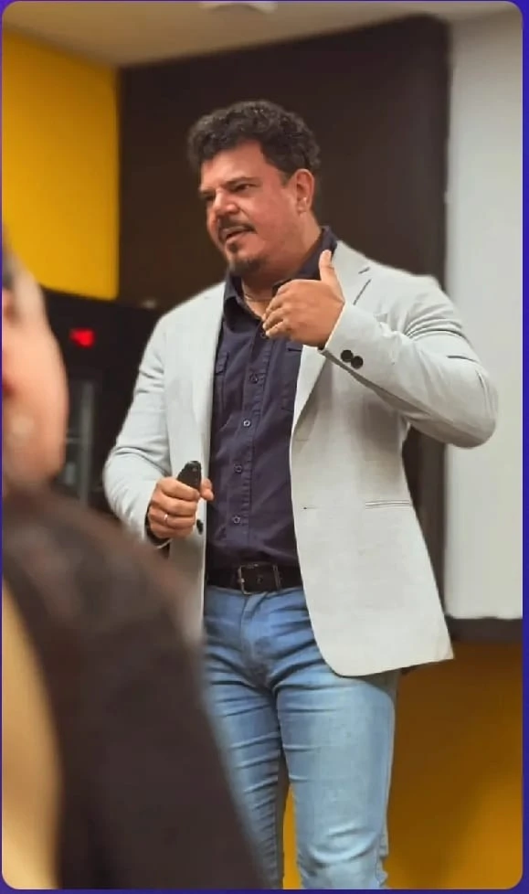 Adriano de pie, con un micrófono en la mano, gesticulando frente a una persona.